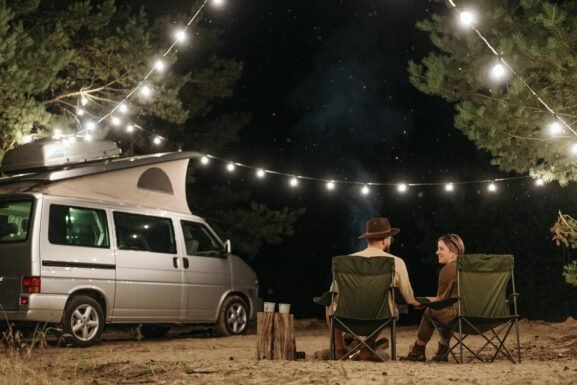 Camping guests relaxing next to a campervan at night under lights